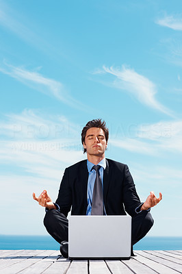 Business man sitting in lotus position with laptop on a pier