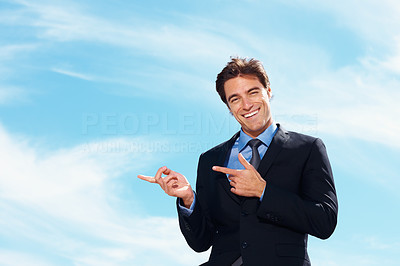 Business man showing something imaginary against cloudy sky