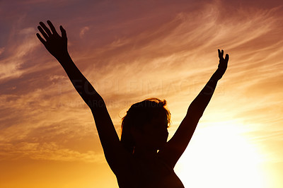 Silhouetted woman with arms raised against scenic sky at sunset