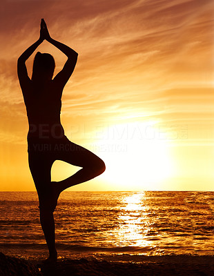 Silhouette image of a woman in tree pose by sea at sunrise