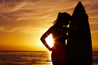 Silhouetted woman with surfboard against scenic sunset by sea