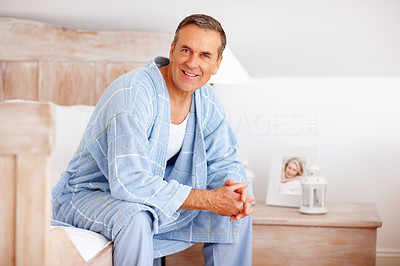 Smiling mature man in bathrobe sitting on bed