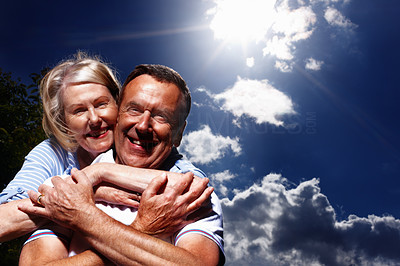 Senior woman hugging husband from behind against cloudy sky