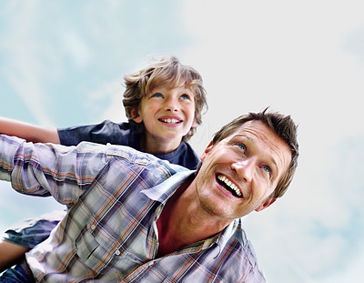 Cheerful mature man with his son on back flying against sky