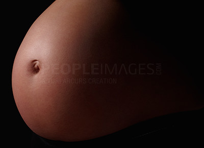 Detail shot of a pregnant woman\'s belly against black