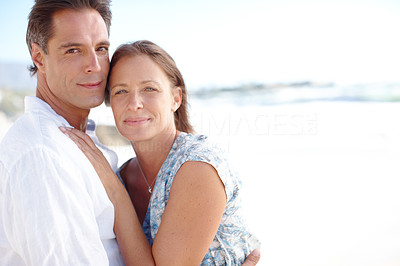 Portrait of a mature man embracing his happy wife from behind as they stand on the beach