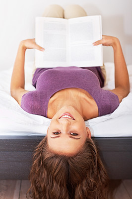 Silly girl holding a book while upside down on bed