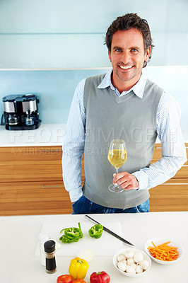Happy mature man holding a glass of wine in kitchen