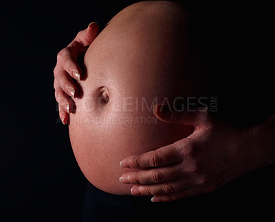 Pregnant woman holding exposed belly against black background