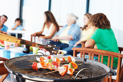 Focus on barbecue with family in background