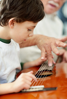 Little boy playing the guitar with help from his grandfather