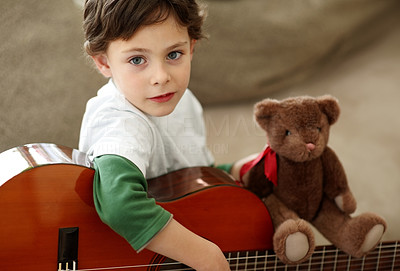 Small boy at home holding a guitar and a teddy bear