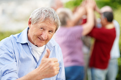 Old man showing thumbs up sign with people in background