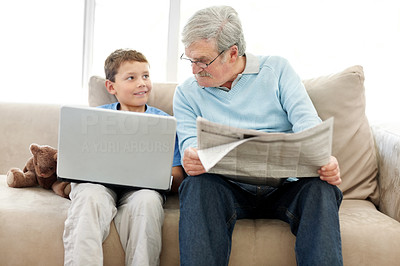 Elderly man sitting with a newspaper while a smiling little boy using a laptop