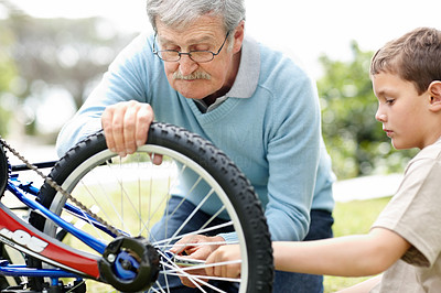 Aged man fixing a bicycle tyre with his grandson in a park