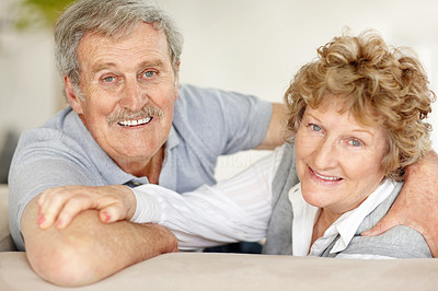 Happy old couple looking behind while sitting on sofa