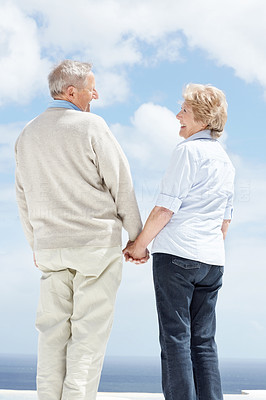 Happy mature couple standing hand in hand against the sky