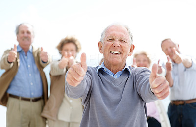 Joyful senior man showing thumbs up sin with his friends at back