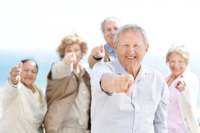 Happy old man pointing at you with his friends in background