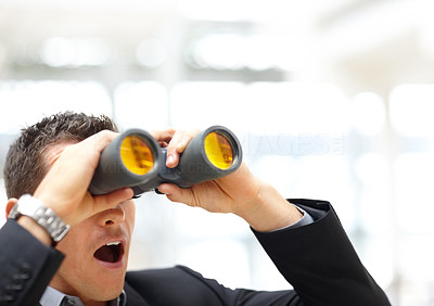 Surprised young business man looking through binoculars