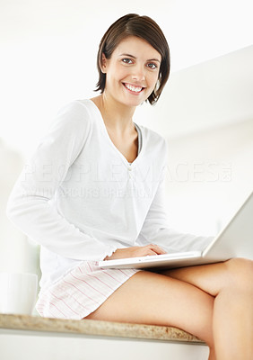 Young female using a laptop while sitting on kitchen counter