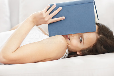 Smiling cute woman covering face with a book while on couch