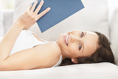 Smiling female reading book while lying on the couch