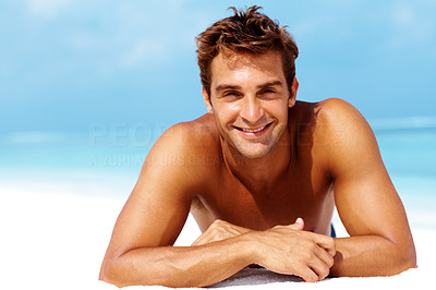 Young man lying on front and smiling at the beach