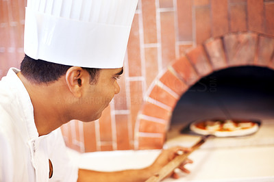 Chef putting pizza in wood fire oven in restaurant