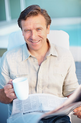 Smiling mature man drinking coffee while reading a newspaper