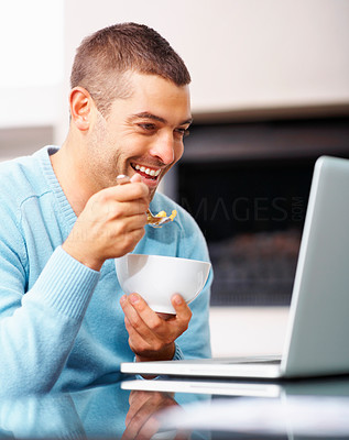 Smiling young guy eating while using laptop