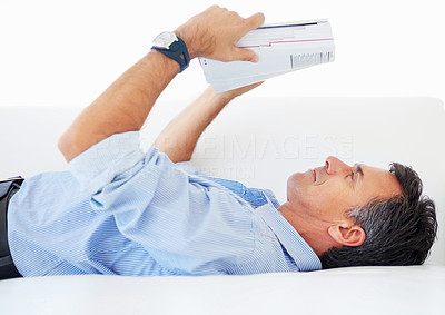 Business man lying on a couch reading a heavy book