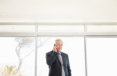 An elderly business man talking over a mobile phone at office