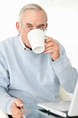 Senior man drinking tea or coffee while working on laptop