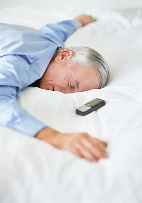 Tired senior man with cellphone lying in bed