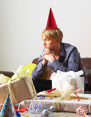 Unhappy man wearing a party hat in a messy living room
