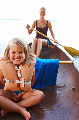 Cute smiling girl sitting in a boat with her mother in background