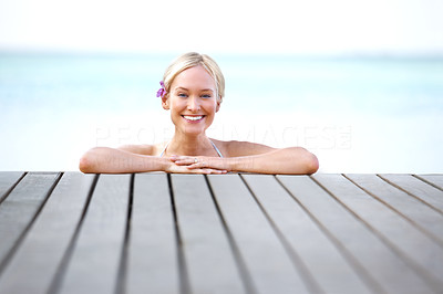Smiling young lady resting on the edge of pier by the sea