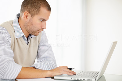 Serious middle aged man holding pen while working on a laptop