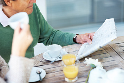 Mature man reading newspaper with wife on breakfast table