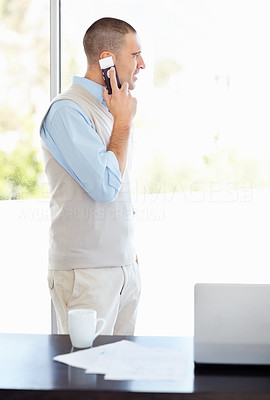 Middle aged man on cellphone with laptop and coffee mug on desk