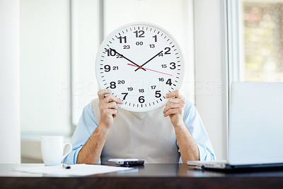 Man covering his face by a wall clock at his desk