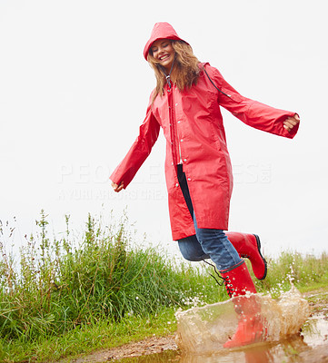 Young female playing in a puddle of water, wearing a red raincoat