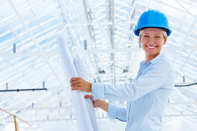 Happy female architect holding blueprint at construction site