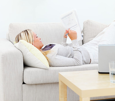 Young woman lying on sofa and writing documents