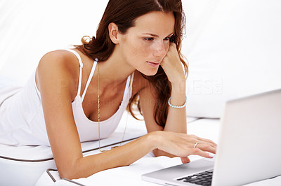 Young caucasian woman lying on bed using laptop
