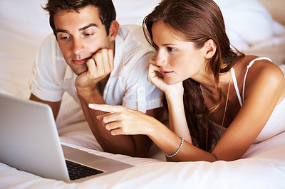 Young couple browsing the internet on a laptop in bed