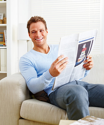 Happy man sitting on couch at home reading newspaper