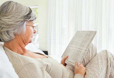 Senior woman reading something interesting newspaper on bed