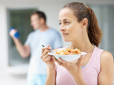 Thoughtful woman eating fruits and man working out at the back